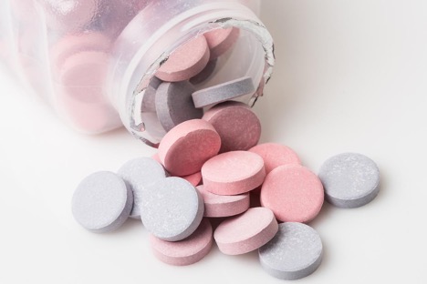 Heartburn pill bottle spilling blue and pink antacid pills on white background Concept of Can I take Pepcid or Prilosec Indefinitely